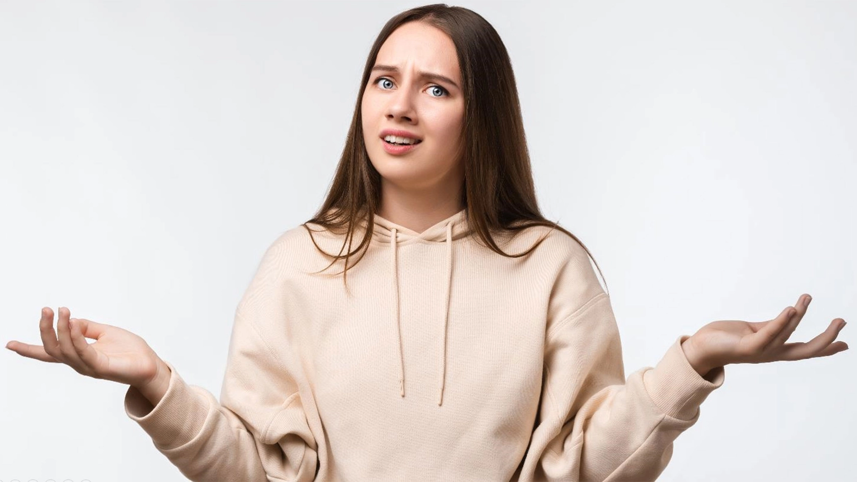  Junge Frau schaut verzweifelt fragend, hebt mit ungläubigen Blick die Hände 