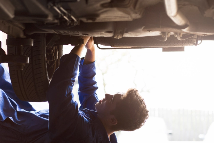 Junger Mann liegt im Blaumann unter repariert etwas am Unterboden.